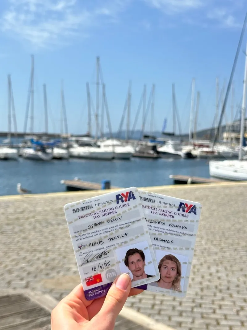 Two RYA Day Skipper certificates held up in front of a marina